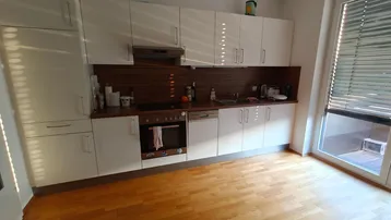 Moderne Küche mit weißen Schränken, Holzarbeitsplatte und Zugang zu einem Außenbereich.