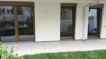 Außenansicht des Erdgeschosses mit kleiner Rasenfläche und gefliester Terrasse.