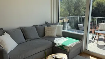 Lichtdurchflutetes Wohnzimmer mit gemütlichem Sofa, Holztischen und Zugang zu einem sonnigen Balkon.