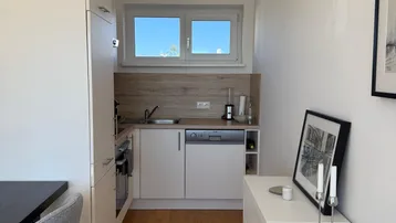 Schmale, moderne Küche mit weißen Schränken, Holzoptik-Arbeitsplatte und Fenster für Tageslicht.
