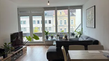 Heller Wohn- und Essbereich mit großen Fenstern, Holzboden und Blick auf die Stadt.