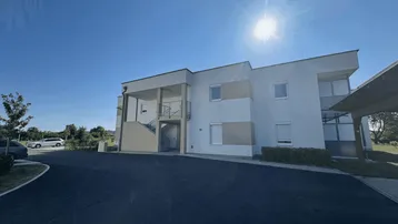 Modernes Mehrfamilienhaus mit heller Fassade und Parkplätzen unter blauem Himmel.