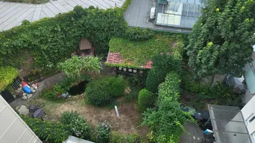 Grüner Innenhof mit Teich, Grillplatz und Sitzgelegenheiten, umgeben von Gebäuden und viel Grün.