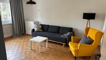 Helles Wohnzimmer mit Parkettboden, bequemer Couch und einem gelben Sessel.