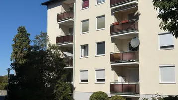 Außenansicht eines Mehrfamilienhauses mit mehreren Balkonen unter blauem Himmel.