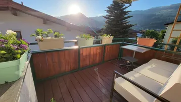 Sonniger Balkon mit Holzboden, bequemen Sitzgelegenheiten und malerischem Bergblick.