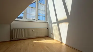 Heller Raum im Dachgeschoss mit Holzboden und Heizkörper, durchflutet von Sonnenlicht.