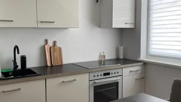 Moderne Einbauküche mit hellen Schränken, dunkler Arbeitsplatte und integriertem Backofen.