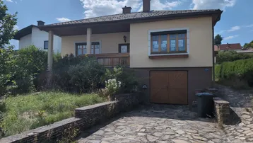 Vorderansicht des Hauses mit Garage, gepflasterter Auffahrt und Gartenbereich unter blauem Himmel.