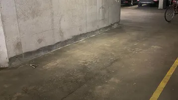 Tiefgarage mit Betonwänden, Asphaltboden und Leuchtstoffröhrenbeleuchtung, bietet Stellplätze für Fahrzeuge.