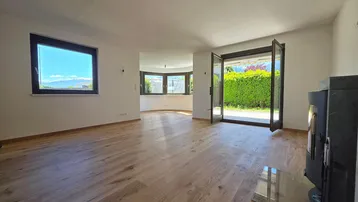 Helles Wohnzimmer mit Holzboden, Kaminofen und Zugang zur Terrasse mit Hecke.