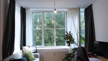 Helles Wohnzimmer mit Sofa, Schreibtisch und großem Fenster mit Blick ins Grüne.