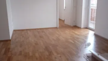 Geräumiges Wohnzimmer mit glänzendem Holzparkettboden und Zugang zu einem französischen Balkon.