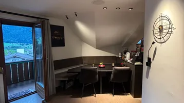 Heller Wohn-Essbereich mit offener Küche, Holzboden und Balkon mit Bergblick.