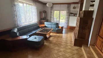 Gemütliches Wohnzimmer mit Parkettboden, Kachelofen und Ledersofas, mit Zugang zum Garten.