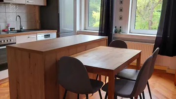 Helle Küche mit Holzboden, integriertem Essbereich und Blick ins Grüne durch große Fenster.