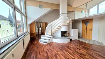 Geräumiges Wohnzimmer mit Holzboden, Kamin und einer eleganten Wendeltreppe, die zur oberen Etage führt.