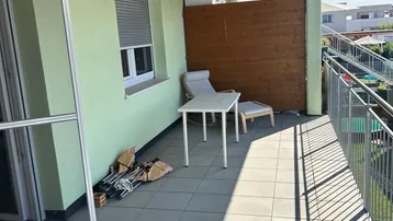 Geräumiger Balkon mit Fliesenboden, Holzdach und Sitzgelegenheiten unter blauem Himmel.
