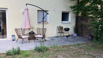 Gemütliche Terrasse mit Gartenmöbeln, Sonnenschirm und Grill, angrenzend an eine kleine Rasenfläche.
