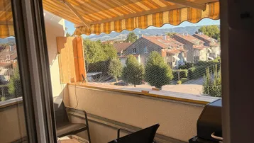 Gemütlicher Balkon mit Markise, Sitzgelegenheiten und Blick auf die umliegende Wohnsiedlung.