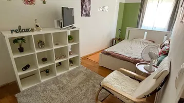 Helles Schlafzimmer mit Holzboden, weißem Regal und einem bequemen Sessel am Fenster.