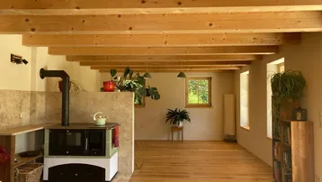Geräumiger Wohnbereich mit Holzbalkendecke, Parkettboden und einem traditionellen Holzofen.