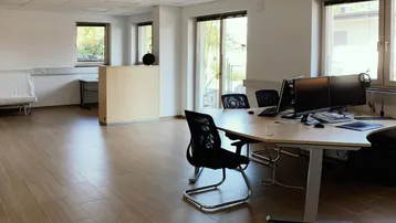 Geräumiges und helles Büro mit modernen Arbeitsplätzen, großen Fenstern und Holzoptik-Fliesenboden.