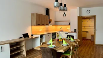 Offener Wohn-Ess-Küchenbereich mit Holztisch, moderner Einbauküche und durchgehendem Holzfußboden.
