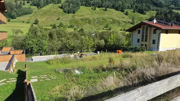 Blick auf die grüne Berglandschaft mit einem Wohnhaus und unbebautem Grundstück im Vordergrund.