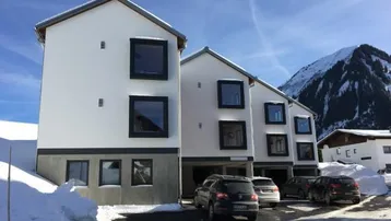 Moderne Mehrfamilienhäuser in den verschneiten Alpen mit Parkplätzen und Bergblick.