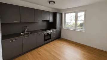 Moderne Küche mit dunklen Schränken, hellem Holzboden und Fenster mit Blick ins Grüne.