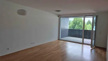 Geräumiges Wohnzimmer mit Holzboden und großem Zugang zu einem Balkon.