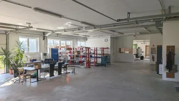 Großer offener Lagerbereich mit Betonboden, vielen Fenstern und Arbeitsplätzen, ideal für gewerbliche Nutzung.
