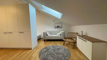 Heller Dachgeschoss-Wohnraum mit Holzboden, Dachfenster und modernen Einbauschränken.