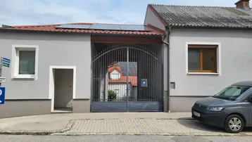 Fassade eines Wohnhauses mit großem Metalltor, Solaranlage auf dem Dach und einem geparkten Auto davor.