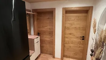 Heller Eingangsbereich mit Holzdecken, Holztüren und einem modernen schwarzen Kühlschrank.