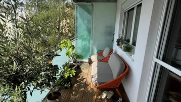 Heller Balkon mit Holzfußboden, Pflanzen und gemütlicher Sitzgelegenheit im Freien.