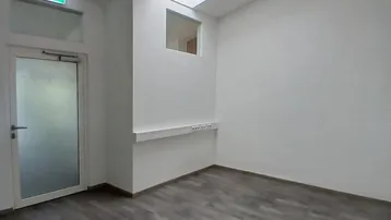 Heller Büroraum mit Laminatboden, hohen Decken und einem Dachfenster für natürliches Licht.