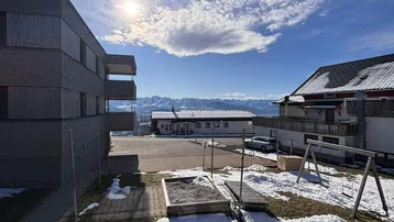 Außenbereich mit Spielplatz, Neubau und Panoramablick auf die Berge im Winter.