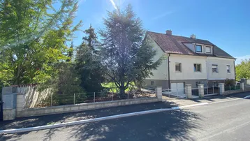 Vorderansicht eines Hauses mit gepflegtem Vorgarten, Einfahrtstor und sonnigem Wetter.