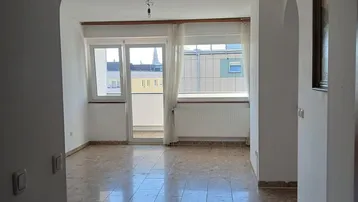 Heller Wohnbereich mit Terrazzoboden und Zugang zu einem kleinen Balkon, durch einen Bogen betretbar.