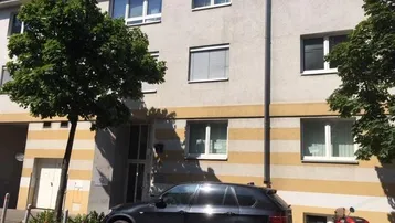 Fassade eines Mehrfamilienhauses mit geparktem Auto und Bäumen davor.