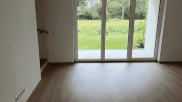 Helles Wohnzimmer mit Laminatboden und großen Fenstern mit Blick ins Grüne.