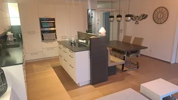 Offener Wohn- und Essbereich mit moderner Einbauküche, Kücheninsel und hellem Parkettboden.