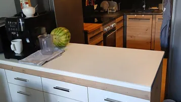 Moderne Küche mit Holzelementen, schwarzer Arbeitsplatte und weißer Kücheninsel, ausgestattet mit Kühlschrank und Kaffeemaschine.