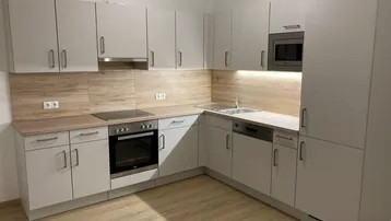 Moderne Einbauküche in Grau mit Holzoptik-Arbeitsplatten und integrierten Geräten.