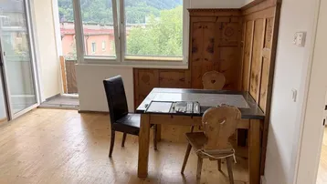 Heller Wohn-Essbereich mit Holzboden, traditioneller Holzvertäfelung und Zugang zum Balkon mit Bergblick.