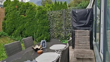 Gedeckte Terrasse mit Esstisch, Gartenmöbeln und Blick auf die umliegenden Berge.