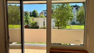 Heller Innenraum mit Zugang zu einem gefliesten Balkon und Blick ins Grüne.