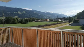 Balkon mit Holzboden und Lattenrost-Geländer bietet weiten Blick auf Berge und grüne Landschaft.
